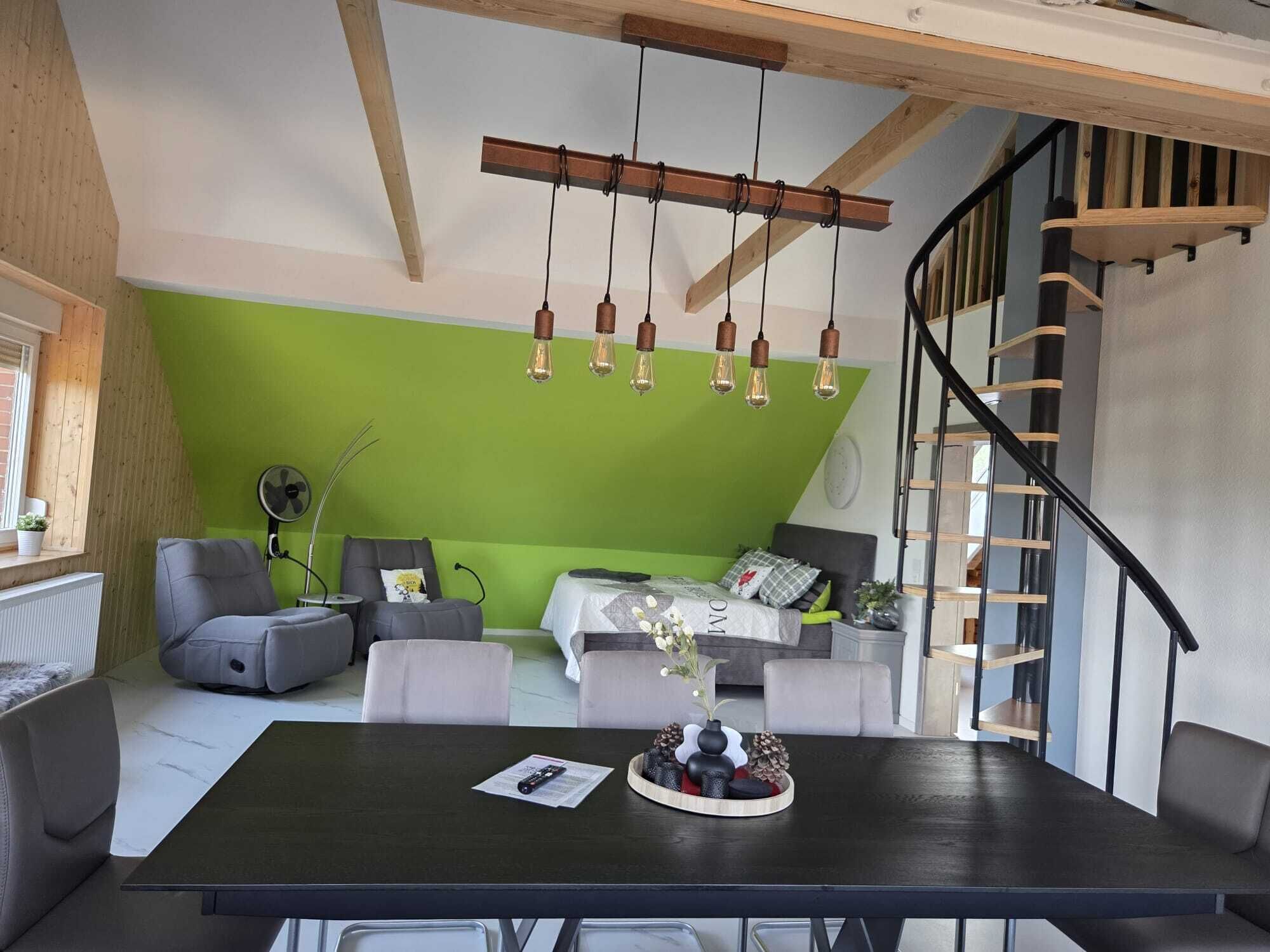 Ein modernes Wohnzimmer mit grüner Akzentwand, Holzboden und einer schwarzen Treppe.
