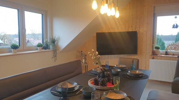 Et spiseområde med et træbord, bænke og et fjernsyn ophængt på væggen.