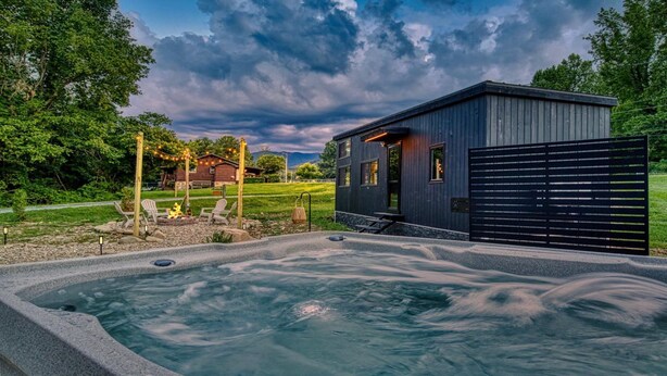 Ein Whirlpoolbereich mit einer Holterrasse und Stühlen, ein kleines Gebäude mit dunkler Fassade und ein großes schwarzes Tor.