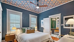 A bedroom with a large bed, two windows with blinds, a ceiling fan, and a nightstand with a lamp. - Hot Tub & Game Room~ Private Cooper-Young Bungalow -Fire Pit - Large Yard (Memphis)