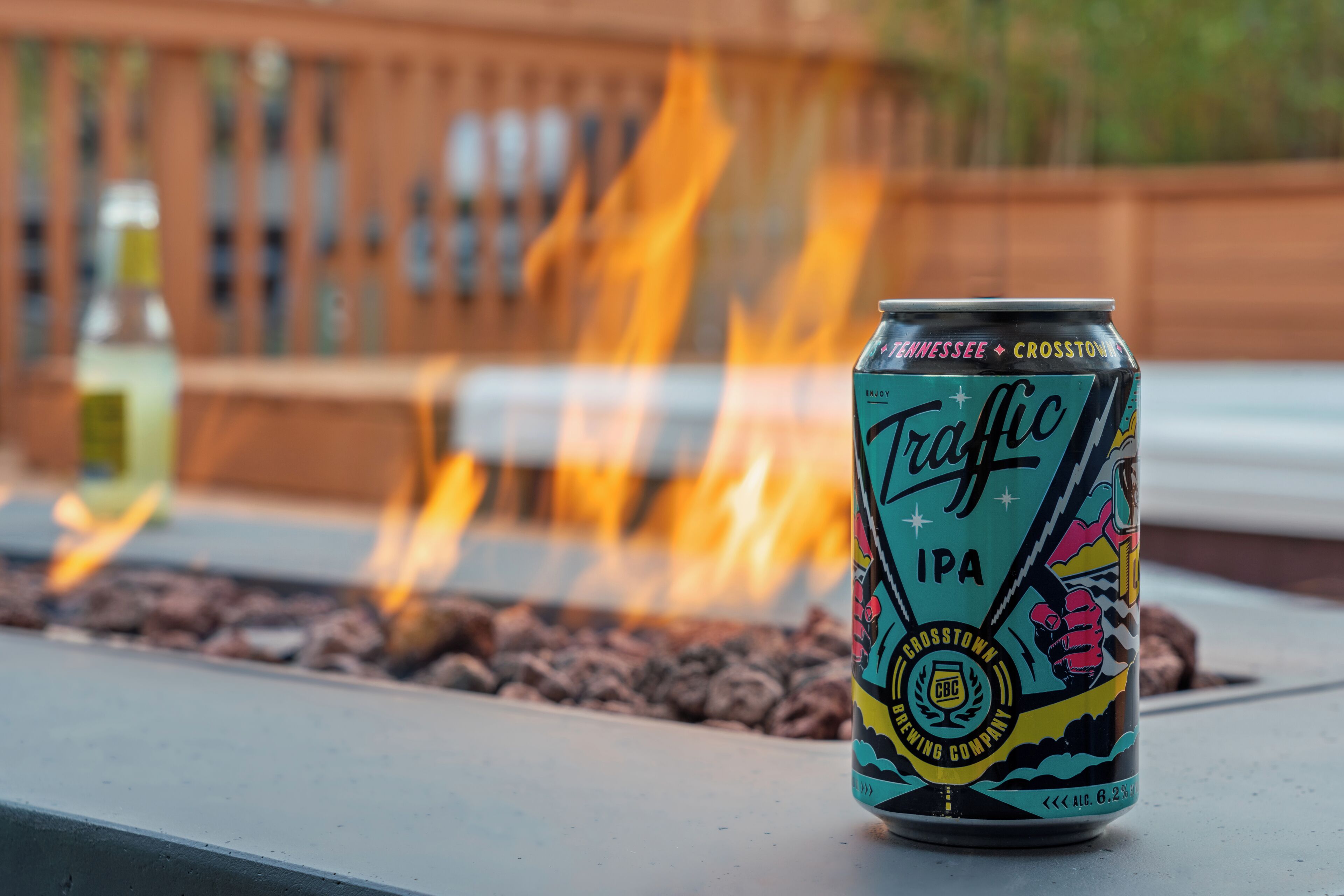 A can of Traffic IPA beer with a colorful label, placed on a surface with a fire in the background.