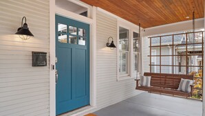 A porch with a blue door, a swing, and a bench. - Hot Tub & Game Room~ Private Cooper-Young Bungalow -Fire Pit - Large Yard (Memphis)