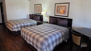Een hotelkamer met twee bedden, een bureau, een stoel en twee ingelijste foto’s aan de muur.
