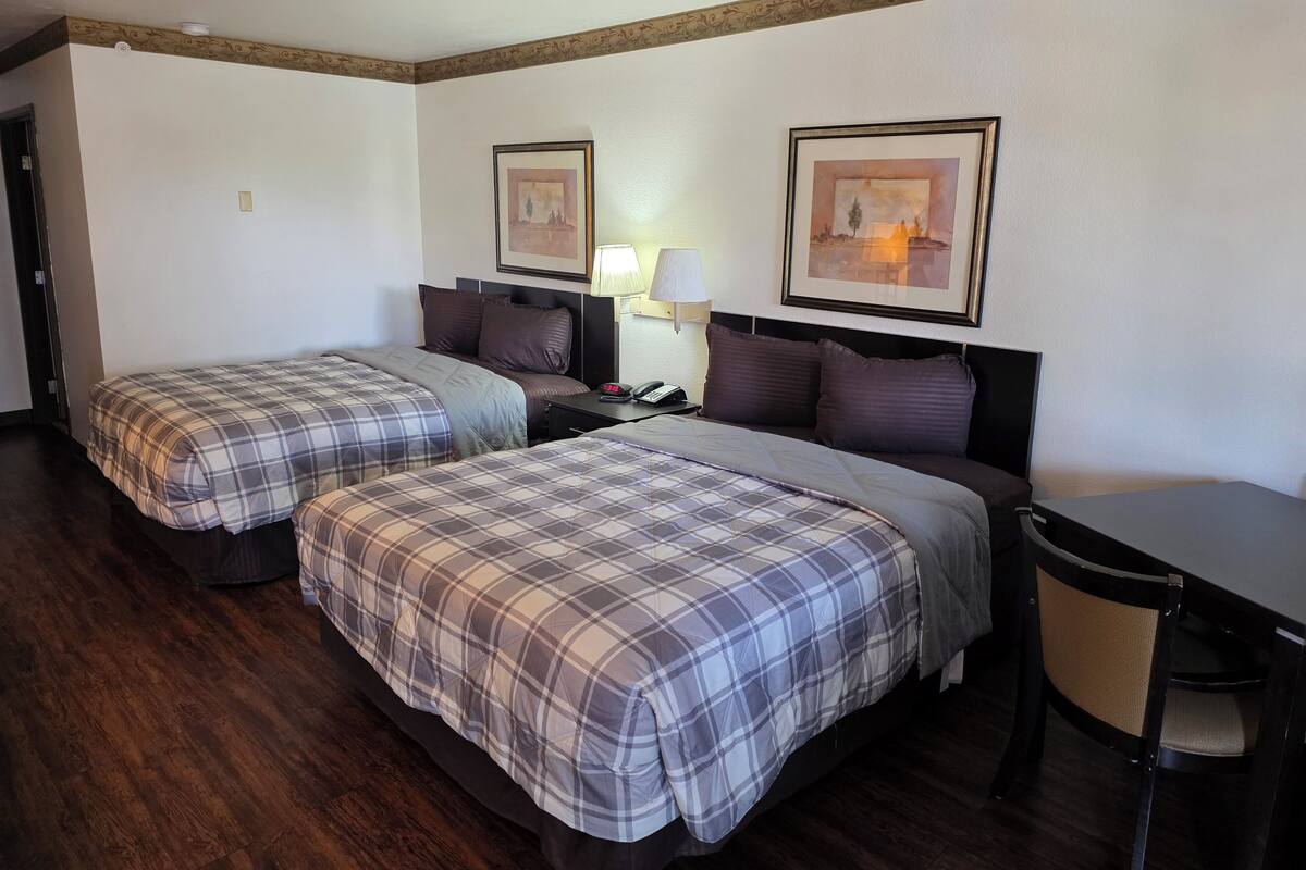 Una habitación de hotel con dos camas, un escritorio, una silla y dos cuadros en la pared.