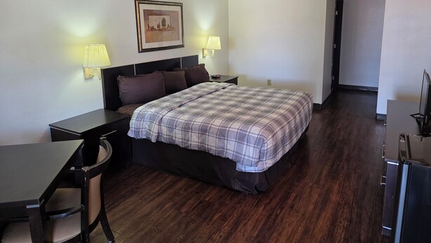 Een hotelkamer met een bed, een bureau, twee bedlampjes, een lijst met foto aan de muur en een televisie op een standaard.