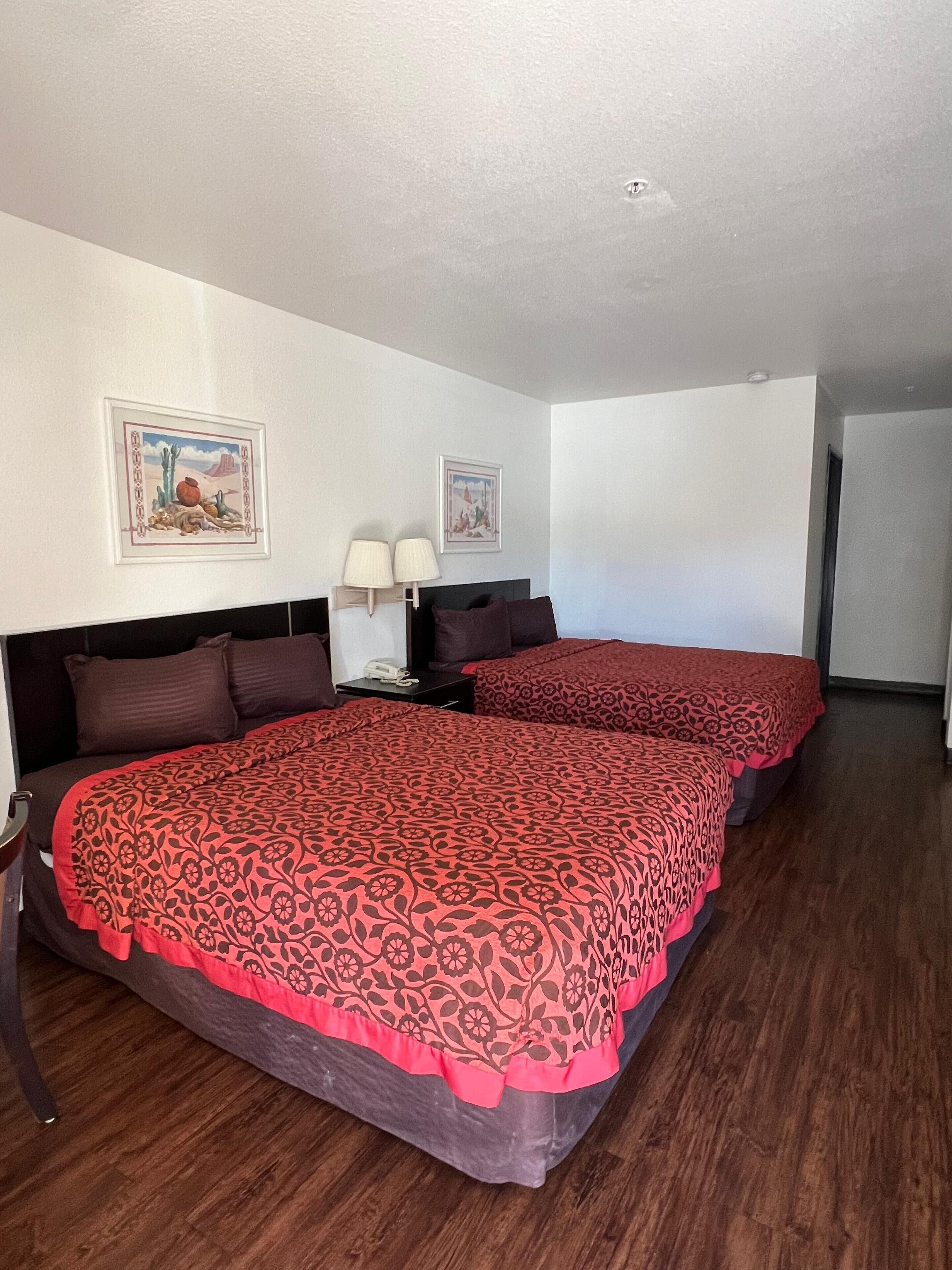 A hotel room with two beds, a nightstand, two wall-mounted lamps, and two framed pictures on the walls.