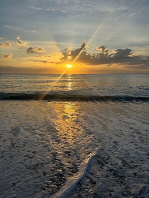 Ein Strand bei Sonnenuntergang mit Wellen und wolkenlosem Himmel.