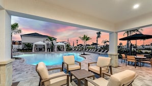 Zona de piscina con sillones reclinables y mesas, un espacio de estar cubierto, y vistas a la piscina y el paisaje circundante.