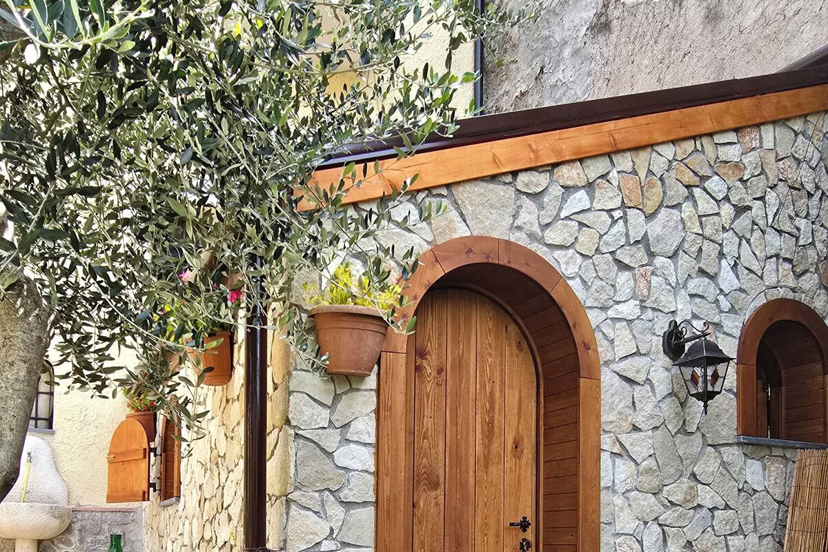 Un edificio de piedra con puerta de madera y ventanas arqueadas, rodeado de macetas con plantas y un sendero de piedra.