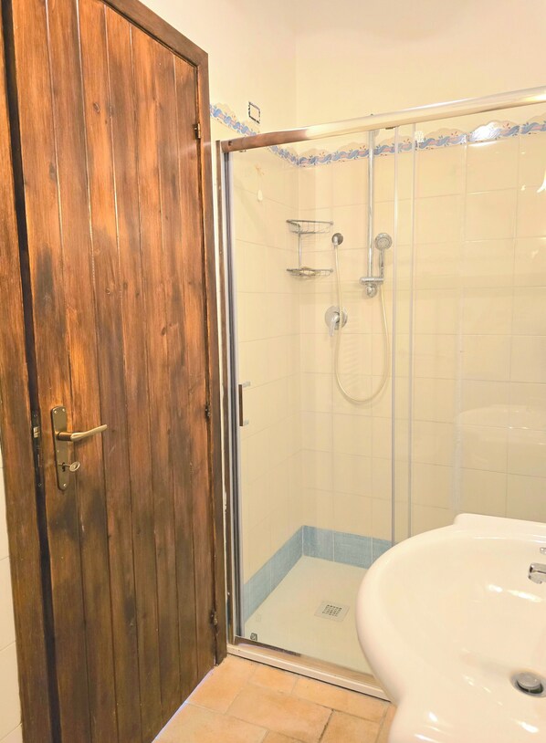 Un baño con puerta de madera, cabina de ducha con vidrio y lavamanos blanco.