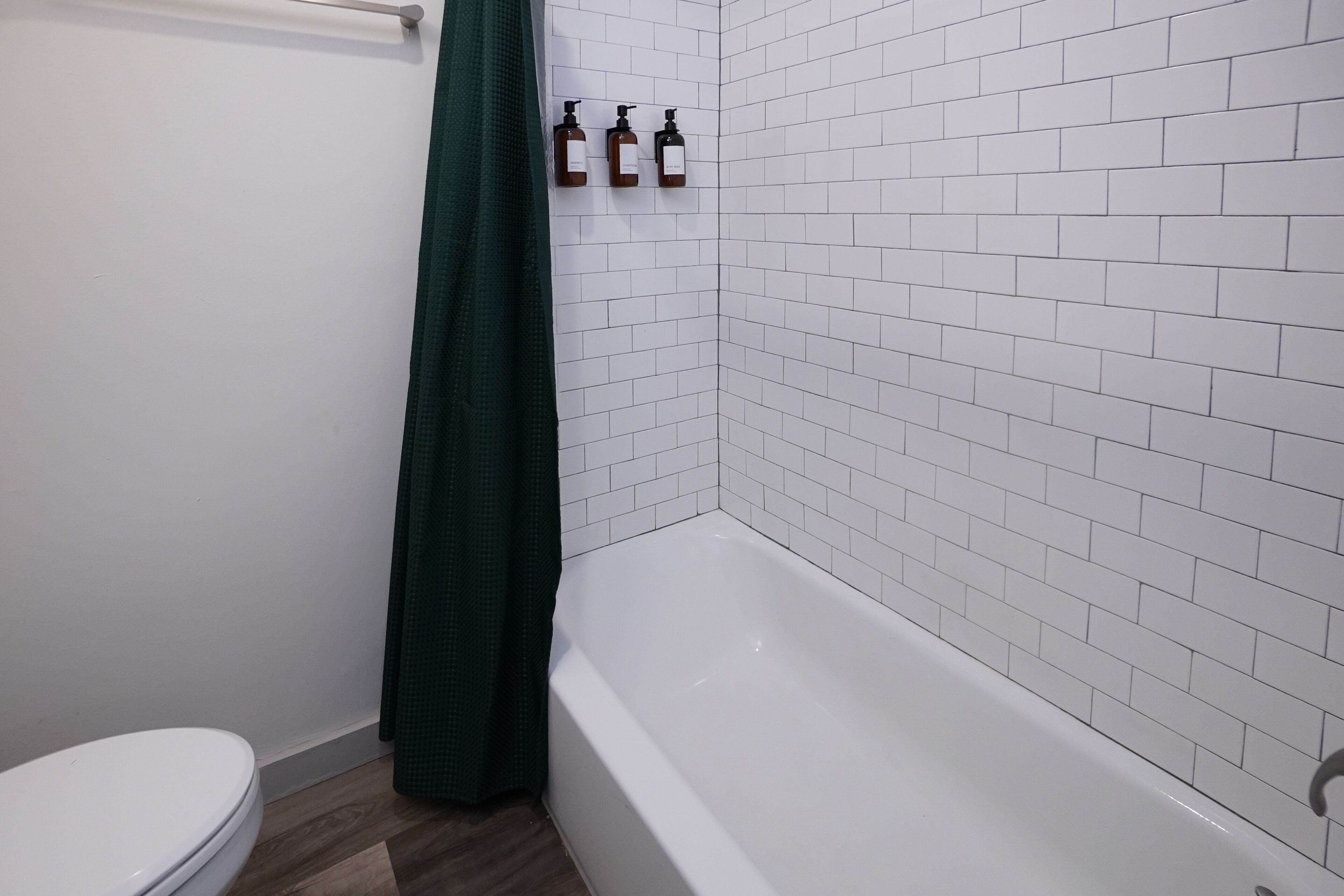 A bathroom with a white toilet, a bathtub, and three bottles of liquid soap on the wall.
