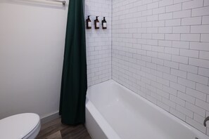 Ein Badezimmer mit Toilette, Badewanne und drei Flaschen Flüssigseife an der Wand.