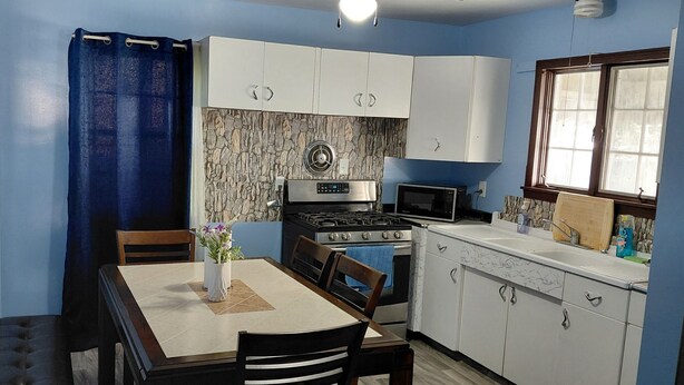 Una cocina compacta con gabinetes blancos, estufa, microondas y una mesa de comedor con sillas.