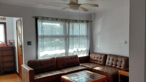 Una sala de estar con un sofá de cuero marrón, una mesa de centro de vidrio y un ventilador de techo.