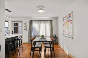 Un comedor con mesa, sillas y ventana con cortinas.