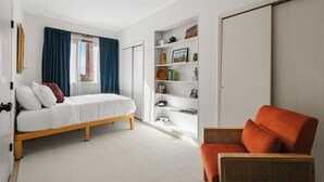 Un dormitorio con cama, una silla, una estantería y un armario.