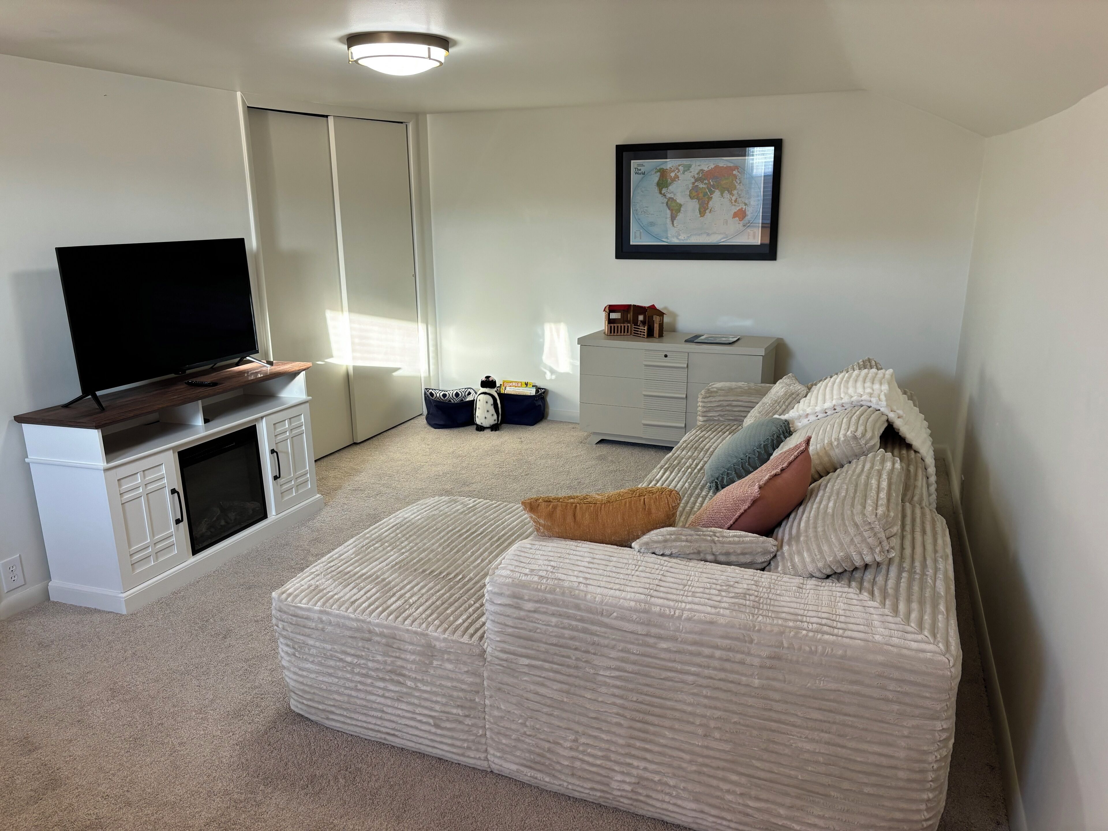A living room with a TV on a stand, a sofa, a coffee table, a dresser, and a world map on the wall.