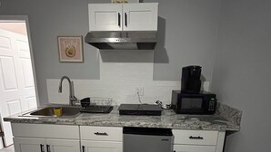 A compact kitchen with white cabinets, a stainless steel range hood, a microwave, and a dishwasher.