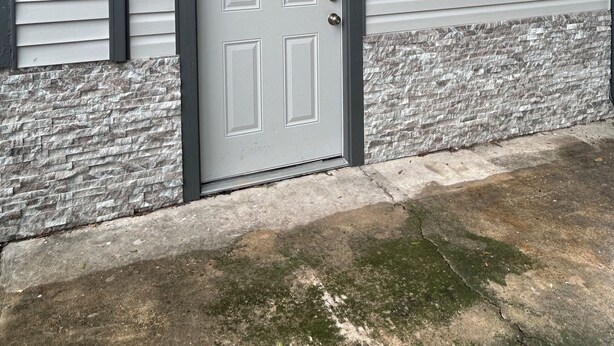 A house with a grey door, two exterior wall-mounted lights, and a stone baseboard.