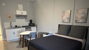 A bedroom with a bed, a desk, and a kitchenette.