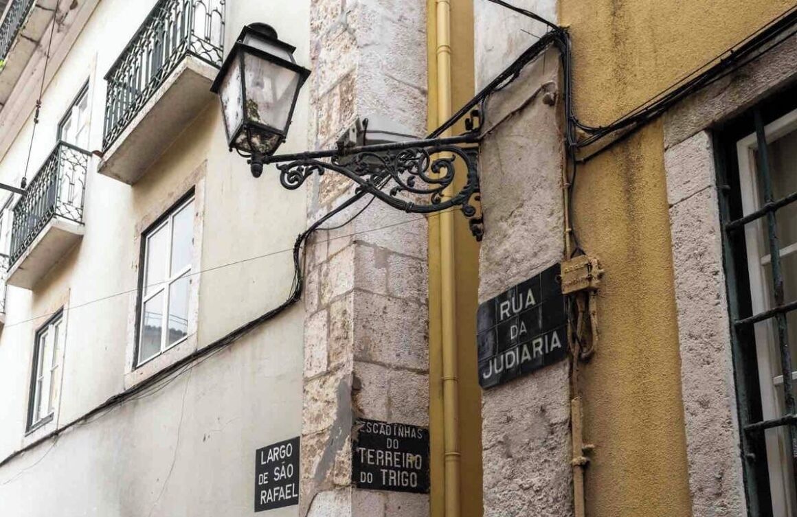 Una señal de calle que indica Rua da Judaria y un poste de luz en la fachada de un edificio.