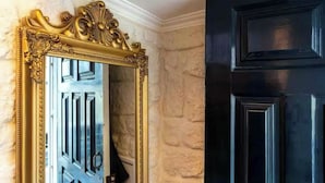 A room with a large ornate mirror, a black door, and a stone wall.
