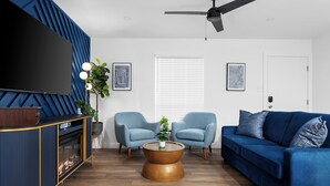 A modern living room with a blue sofa, two armchairs, a coffee table, a TV, and a ceiling fan. - Premier Access Zilker Park & SoCo (Austin)