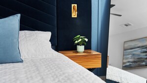 A bedroom with a bed, a bedside table with a plant, a wall-mounted light, and a painting on the wall. - Premier Access Zilker Park & SoCo (Austin)