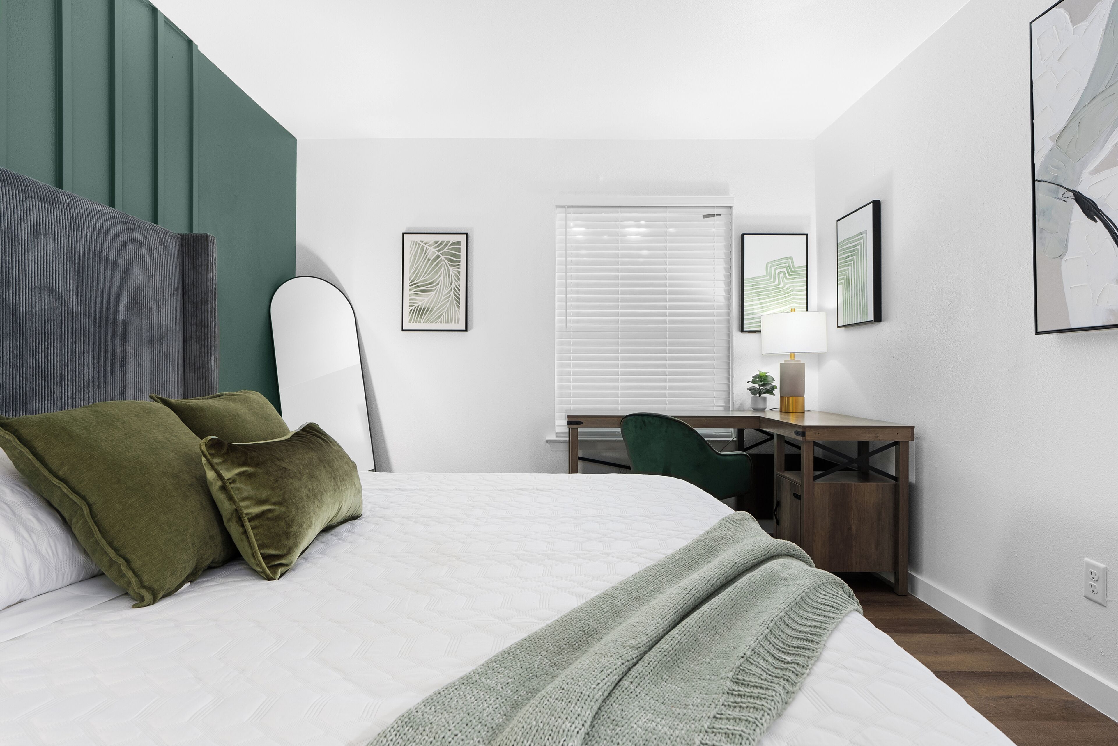 A modern bedroom with a bed, green pillows, a desk, and a chair.