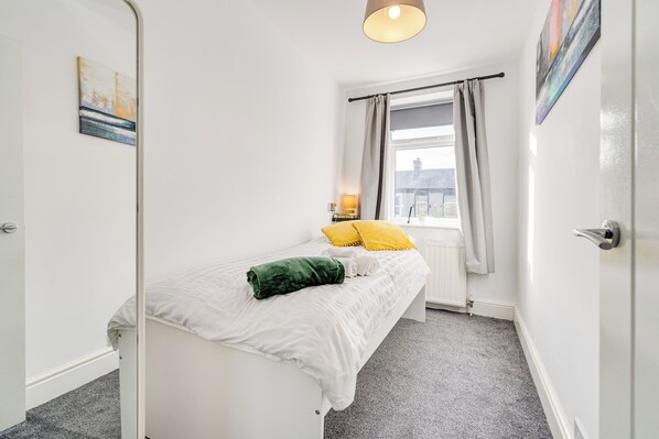 A bedroom with a bed, a window with curtains, a radiator, and a painting on the wall.