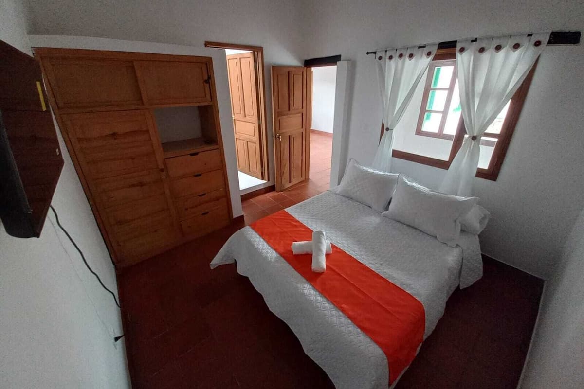 Un dormitorio con cama, armario de madera y ventana con cortinas.