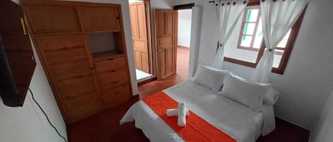 A bedroom with a bed, a wooden wardrobe, and a window with curtains.