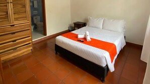 Un dormitorio con una cama, un armario de madera y un baño visible a través de una puerta abierta.