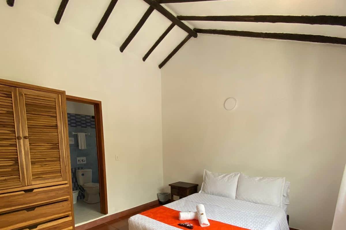 Un dormitorio con una cama, un armario de madera y un baño visible a través de una puerta abierta.