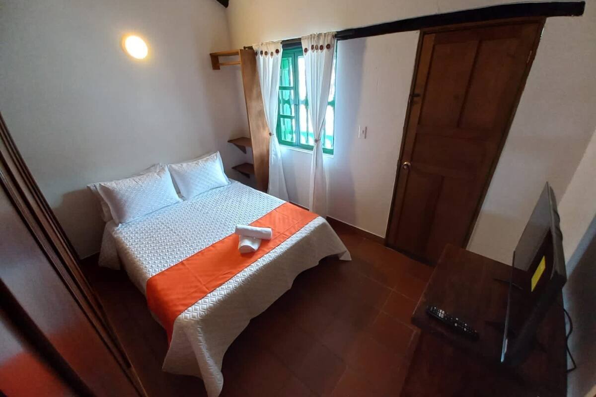 Un dormitorio con una cama, un armario de madera, un televisor y una ventana con cortinas.