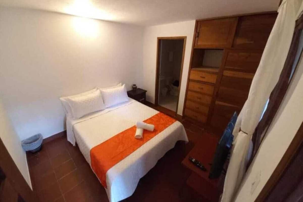 Una habitación de hotel con una cama, una mesita de noche, un armario y la puerta del baño.