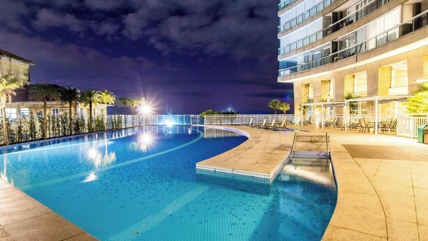 A nighttime swimming pool with a curved design, surrounded by a white fence and palm trees. - Perfect apartment in the best building on the waterfront with an unobstructed view of the incredible sea! (José Menino Santos)