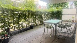 A covered patio with a table and chairs, surrounded by potted plants and a stone wall. - Central, family-friendly apartment with terrace and underground garage in Essen (Essen)