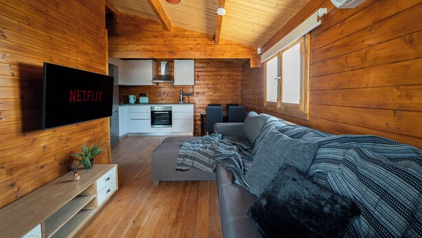 A cozy cabin interior with a wooden interior, a living area with a sofa and a TV mounted on the wall, and a kitchen area with cabinets and a stove. - KTIMA TO ALLIOTIKO - LOFOU 1 - 4 BDR VILA
LIMASSOL - CYPRUS
ENJOY FANTASTIC VAC (Lofou)