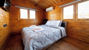 A wooden cabin room with a bed, two windows, an air conditioning unit, and a television mounted on the wall. - KTIMA TO ALLIOTIKO - LOFOU 1 - 4 BDR VILA
LIMASSOL - CYPRUS
ENJOY FANTASTIC VAC (Lofou)