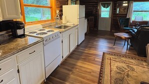 Une cuisine spacieuse avec un plancher en bois, des armoires blanches et une grande fenêtre donnant sur un espace verdoyant.