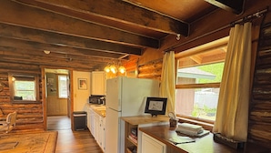 Une cuisine chaleureuse, aménagée dans le style d’un chalet, avec un plancher en bois, un réfrigérateur, un évier et un coin bar équipé de tabourets.