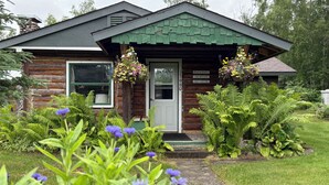 Une cabane en rondins avec un toit recouvert de bardeaux verts, une porte d’entrée et un petit porche.