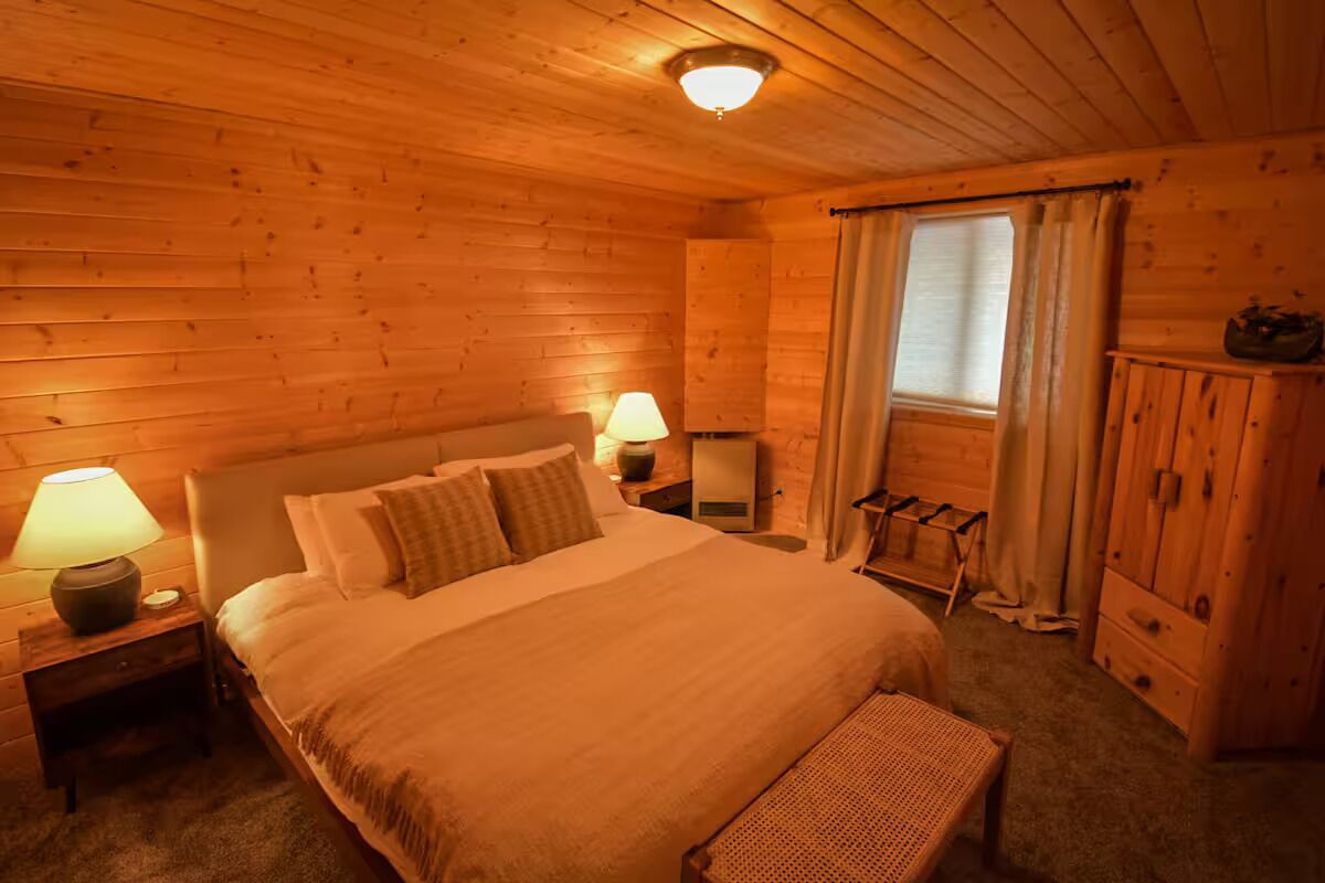 Ein gemütlicher Holzraum mit einem großen Bett, zwei Nachttischlampen, einer Bank und einem Kleiderschrank.