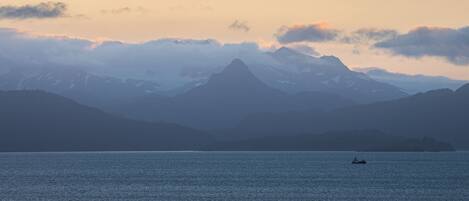 A calm lake with a boat in the distance, surrounded by mountains and a clear sky.