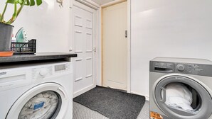 Ett tvättrum med en tvättmaskin med frontmatning, en torktumlare, en krukväxt och en dörr med lås.