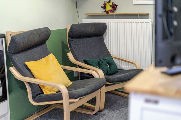 Two reclining chairs with cushions, a wooden desk, and a radiator in the background.