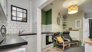 Ett modernt kök med vita skåp, en svart bänkskiva och en grön accentvägg. Det finns en stol med en gul sittkudde och en hängande lampa.