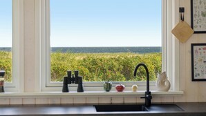 Une cuisine avec une fenêtre donnant sur un champ, un évier et un plan de travail sur lequel sont posés des ustensiles de cuisine.