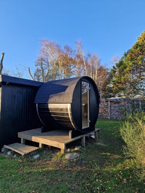 Een cilindervormige houten constructie met een glazen deur, een houten terras en een stenen muur op de achtergrond.